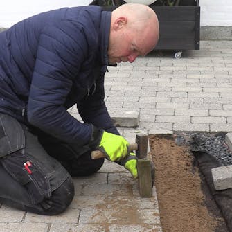 Fliserne skrider: Brug en træklods og en hammer til at banke fliserne på plads Fliserne skrider: Brug en træklods og en hammer til at banke fliserne på plads